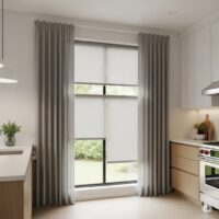 A modern kitchen interior featuring light gray roller blinds combined with sheer curtains, creating a stylish and functional window treatment.